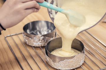 Woman's hands pouring cake batter into cake mold, ready to bake.