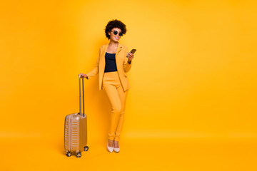 Full size photo of focused brown wavy hair tourist girl use smartphone hold bag try book taxi reach destination on autumn weekends wear jacket pants high-heels isolated yellow color background - obrazy, fototapety, plakaty