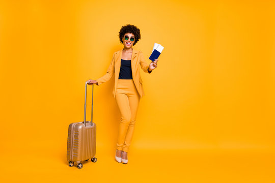 Full length photo of positive brown curly hair lady hold trolley package ready to enjoy summer perfect weekends wear style jackets trousers high heels isolated over yellow color background