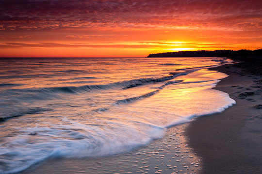 Sunrise at sandy beach in Baabe, slow incoming waves, morning sky with orange sunrise, Ruegen island, Baltic Sea, Germany.