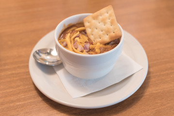 A bowl of spicy chili and crackers with a spoon.