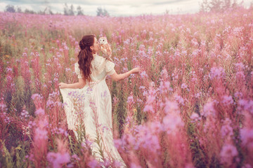 Woman with owl on her shoulder go away to field of pink flowers.