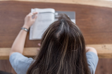 Fototapeta premium Top view of young woman reading a book in a lounge, cafe on a wood table.
