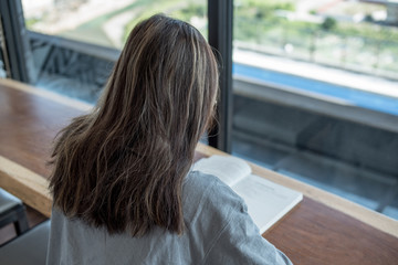 Young woman reading a book in a lounge, cafe near large windows.