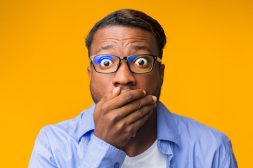 Shocked African American Guy Covering Mouth With Hand, Yellow Background