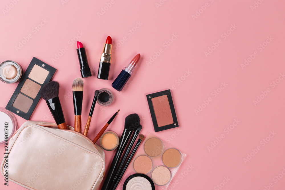 Wall mural a pink makeup bag with cosmetic beauty products spilling out on to a pastel colored background, with