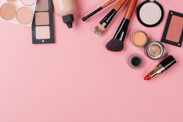 A pink makeup bag with cosmetic beauty products spilling out on to a pastel colored background, with empty space at side