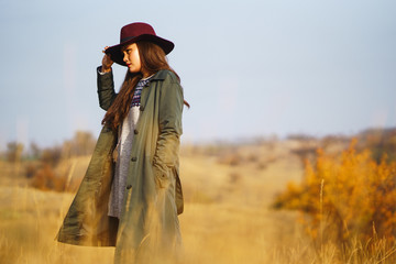 Beautiful young stylish girl in a coat walks in the autumn in the park. The girl is dressed in a green coat and a red hat. Beautiful evening. Autumn fashion. Lifestyle. High fashion portrait.