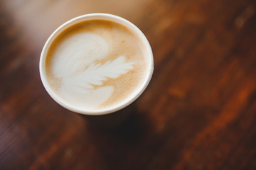 Top view texture of foam and coffee cappuccino latte bubbles in paper cup on wooden table, lens flare