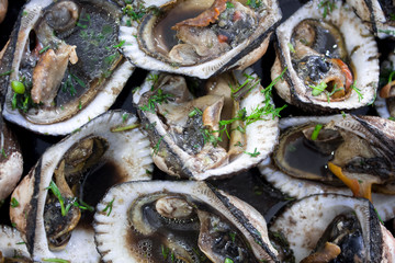 Close-up seafood: steamed clams, mussels, or oysters served in a plate on a black marble table. Clams showing meat, oil, and herbs. Delicious ecuadorian seafood platter.