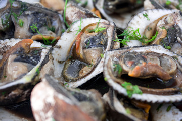 Close-up seafood: steamed clams, mussels, or oysters served in a plate on a black marble table....