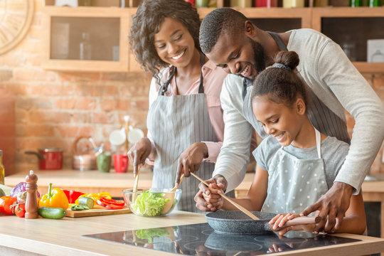 Afro parents teaching their daughter how to cook