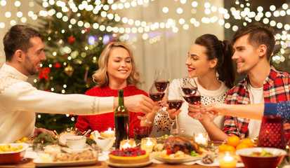 holidays and celebration concept - happy friends having christmas dinner at home, drinking red wine and clinking glasses