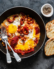 Shakshuka with baked sweet peppers and chickpeas in frying pan on a dark background, top view