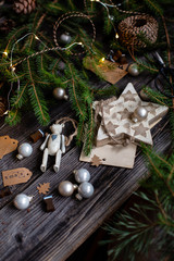 christmas grey ball toys, teddy bear, wooden star on rustic wooden table with fir tree branches, tags, striped threads and bright garland
