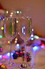 Glasses with champagne on a beautiful background of bright Christmas holiday lights. Christmas colorful toys for spruce. Photo with purple and yellow. 