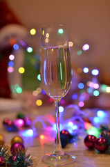Glasses with champagne on a beautiful background of bright Christmas holiday lights. Christmas colorful toys for spruce. Photo with purple and yellow. 