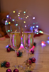 Glasses with champagne on a beautiful background of bright Christmas holiday lights. Christmas colorful toys for spruce. Photo with purple and yellow. 