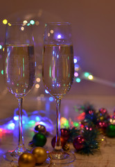 Glasses with champagne on a beautiful background of bright Christmas holiday lights. Christmas colorful toys for spruce. Photo with purple and yellow. 