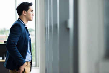 Fototapeta premium Portrait of a cheerful mature asian young businessman wear a business suit of man in blue jacket and blue shirt looking at the window In the office room background.
