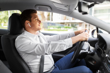 transport, vehicle and people concept - man or driver with wireless earphones or hands free device driving car
