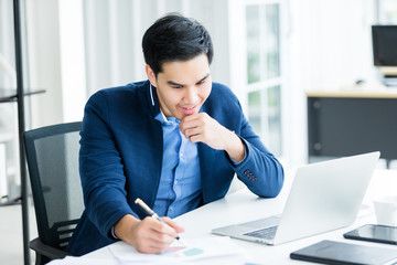 Happy mood a cheerful of asian young businessman have ideas make a note the successful business plan in document paper and laptop computer on wooden table background in office.