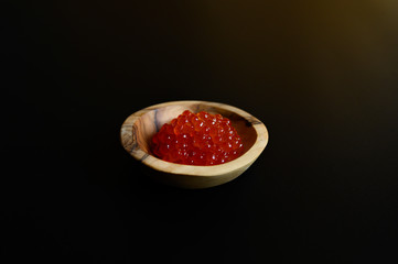 red salmon caviar in a small wooden plate made of olive wood