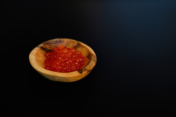 red salmon caviar in a small wooden plate made of olive wood, space for text