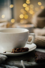 Cup of coffe with milk and chocolate cookies on warm wool blanket, cozy winter home
