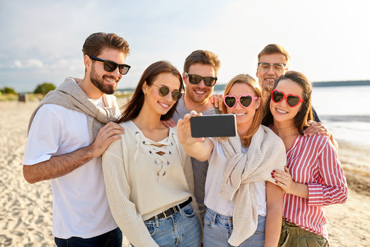 friendship, leisure and people concept - group of happy friends taking selfie by smartphone on beach in summer