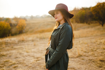 Beautiful young stylish girl in a coat walks in the autumn in the park. The girl is dressed in a green coat and a red hat. Beautiful evening. Autumn fashion. Lifestyle. High fashion portrait. 