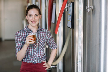 Portrait of confident young woman holding beer glass at a brewery
