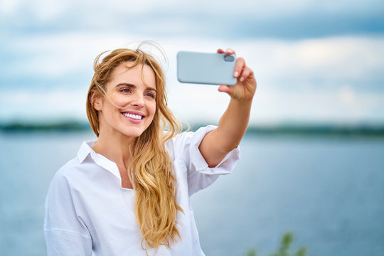 Happy woman taking selfie with smartphone at the lakeside