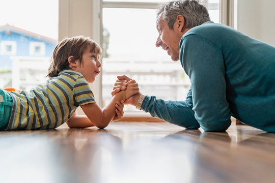 Father and son lying on the floor at home arm wrestling