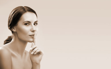 Brown tone vintage style beauty portrait of young woman keeping finger on her lips and asking to keep quiet