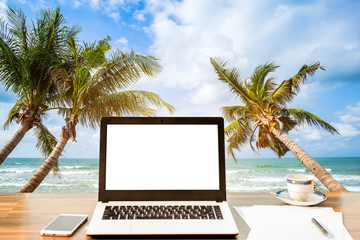 Mockup of laptop computer with empty screen with smartphone and coffee cup on wooden on table at landscape early sunrise over blue the sea background,working on the beach,Freelance work and holiday