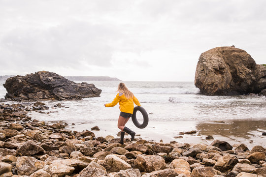 Woman wearing yellow rain jacket with floating tire, walk aon rocky beach
