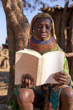 Traditional muhila woman, sitting under tree, reading a book, Kehamba, Chibia, Angola