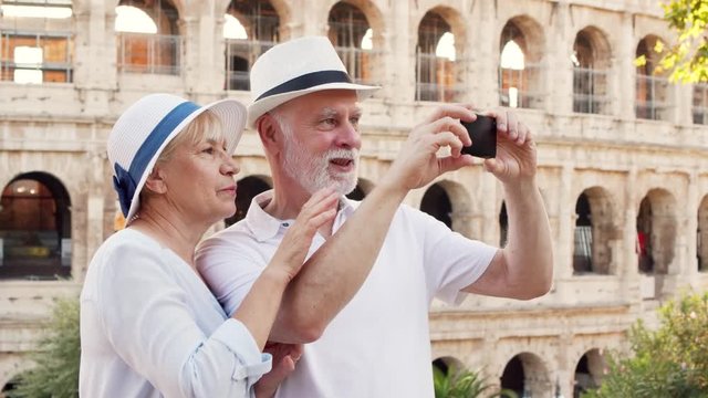 Happy tourists family in hats enjoy vacation in Rome, Italy. Senior couple take photo with mobile phone near famous Italian attraction Colosseum. Having fun travelling together