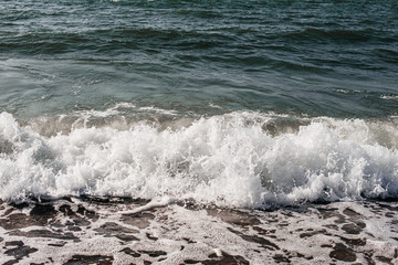 White waves on the sea coast - water on the beach on a summer day