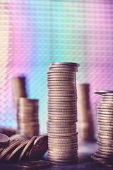 Stacks of golden coins against a disco style background, shallow depth of field, color toning applied.