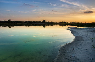 Sandy shore of the azure lake, horizon and colorful sky after sunset
