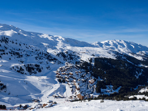 Meribel, France - February, 2018: Wooden Houses in Meribel ski resort. Skiers and snow slopes, beautiful sunny day.