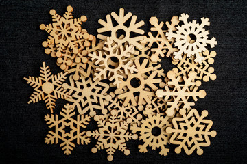 Large group pf delicate light brown wooden snowflakes on dark grey textile material background, displayed centered, top view with space for text around, flat lay with laser cut wooden objects