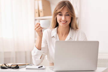 Smiling Businesswoman Holding Coffee Cup Sitting At Laptop In Office