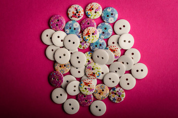 Obraz premium Large group pf delicate light white and painted wooden buttons on dark pink texted cardboard background, displayed centered, top view with space for text around, flat lay