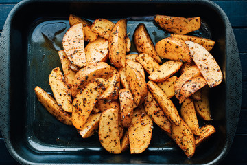 Raw potato wedges with spices and herbs in a baking dish