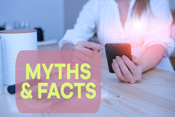 Writing note showing Myths And Facts. Business concept for usually traditional story of ostensibly historical events woman using smartphone and technological devices inside the home