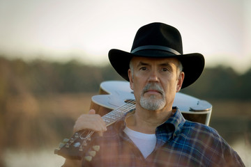 Portrait of a mature man holding an acoustic guitar over his shoulder.