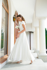 Young elegant woman with wedding bouquet in a light long white dress  before ceremony